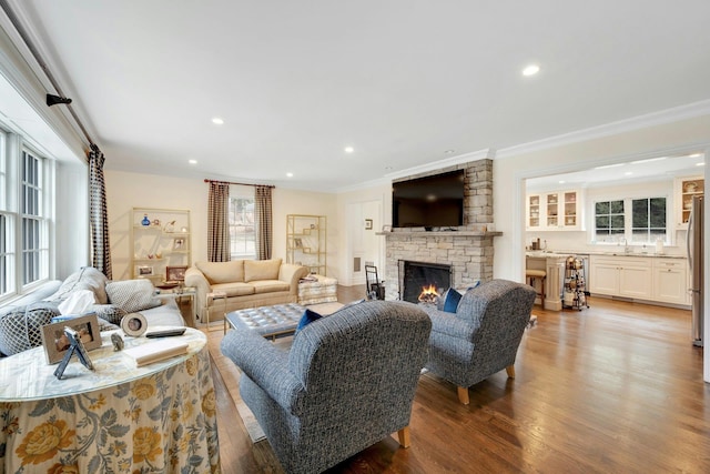 living area with recessed lighting, ornamental molding, wood finished floors, and a stone fireplace