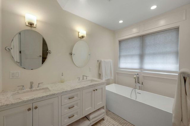 bathroom with double vanity, a freestanding tub, a sink, and recessed lighting