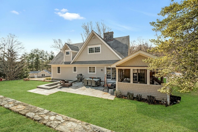 back of property with a shingled roof, a patio area, a lawn, and a chimney