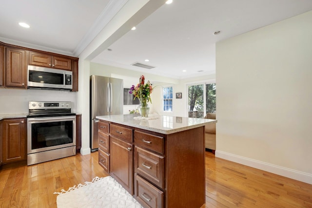 kitchen featuring a center island, light wood finished floors, stainless steel appliances, ornamental molding, and baseboards