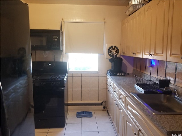 kitchen featuring dark countertops, black appliances, light tile patterned floors, and a sink