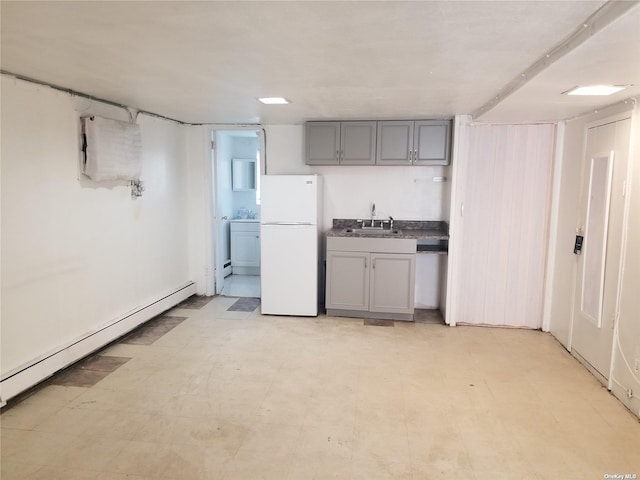 kitchen featuring light floors, baseboard heating, gray cabinetry, freestanding refrigerator, and a sink