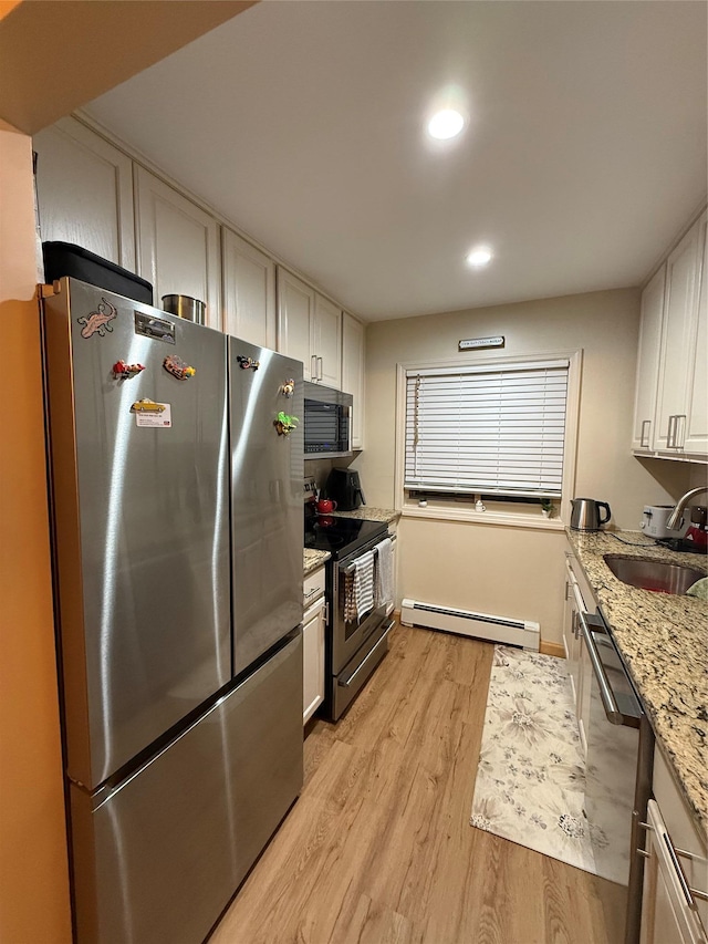 kitchen with light wood finished floors, appliances with stainless steel finishes, a baseboard heating unit, white cabinetry, and a sink