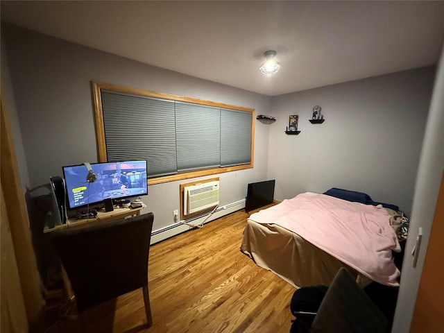 bedroom with a wall mounted AC, baseboard heating, and wood finished floors