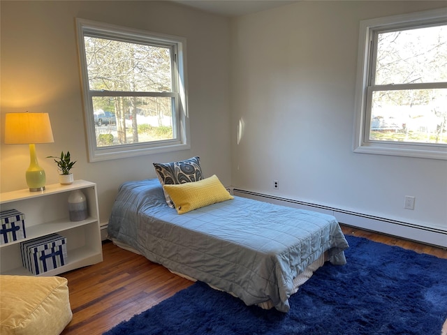 bedroom featuring a baseboard radiator, multiple windows, and wood finished floors