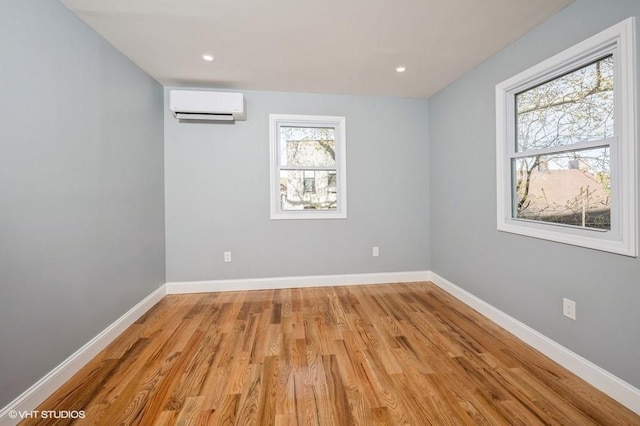 spare room featuring a wall mounted AC, light wood-style flooring, and baseboards