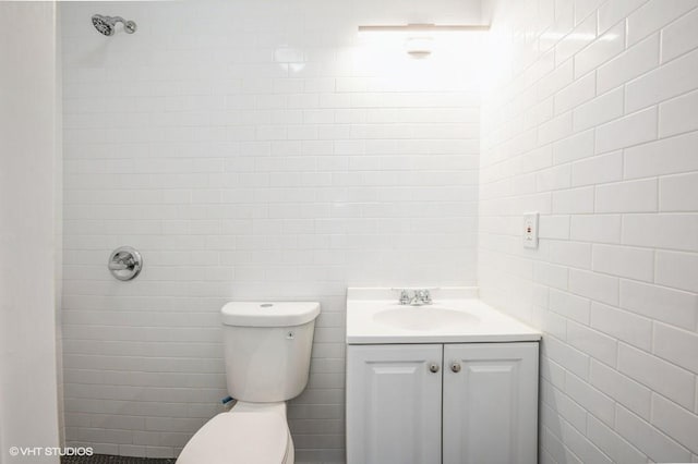 bathroom with toilet, tiled shower, vanity, and tile walls