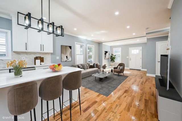 kitchen featuring crown molding, light countertops, backsplash, light wood finished floors, and open floor plan