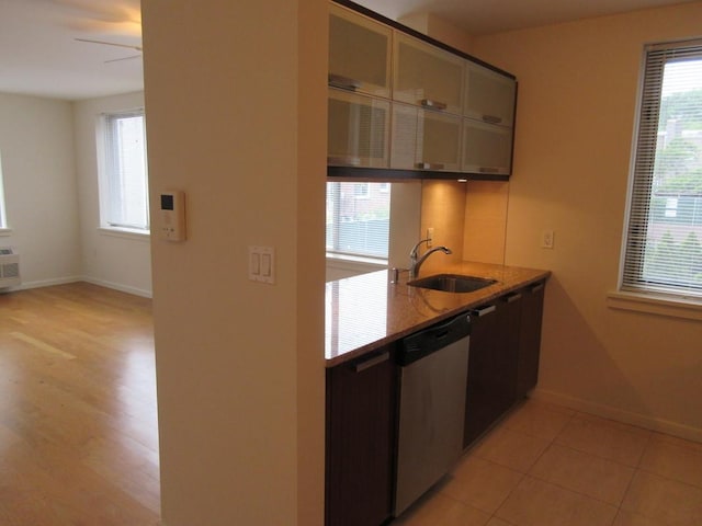 kitchen featuring light stone counters, stainless steel dishwasher, light tile patterned flooring, a sink, and baseboards