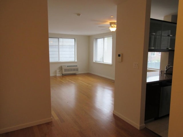 empty room featuring baseboards, a ceiling fan, radiator heating unit, wood finished floors, and a sink