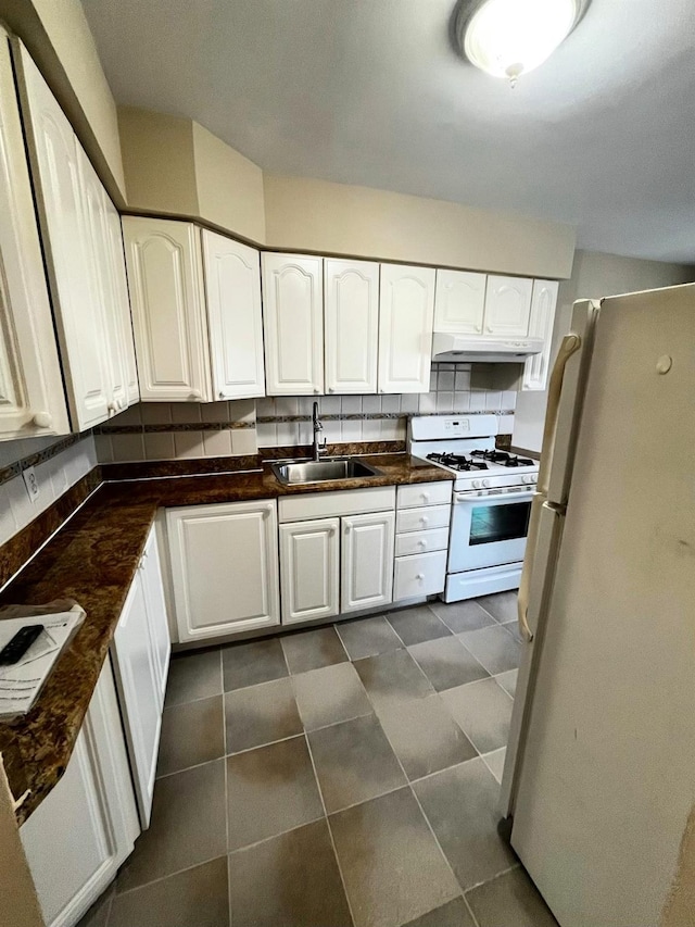 kitchen featuring a sink, under cabinet range hood, dark countertops, white cabinetry, and white appliances