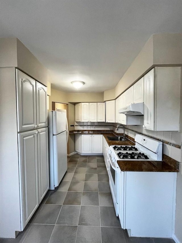 kitchen with dark countertops, under cabinet range hood, decorative backsplash, white appliances, and a sink