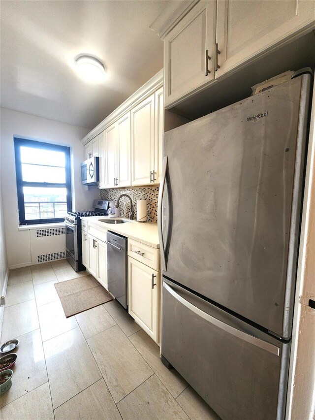 kitchen featuring stainless steel appliances, a sink, light countertops, radiator, and tasteful backsplash