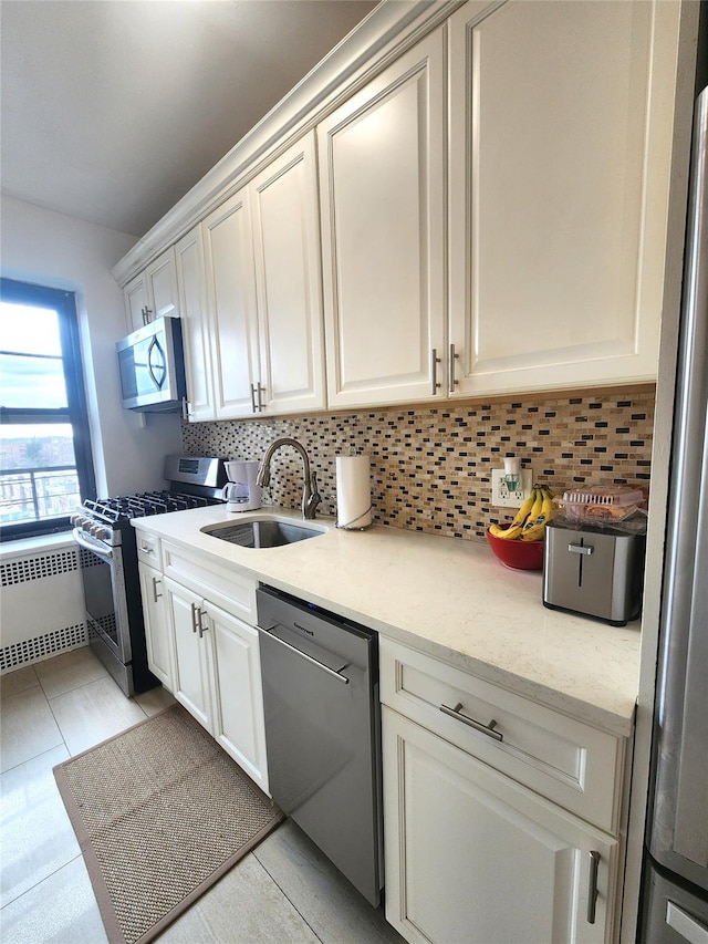 kitchen with stainless steel appliances, a sink, white cabinets, tasteful backsplash, and radiator heating unit