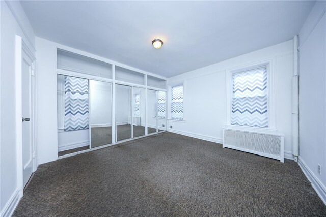 unfurnished bedroom featuring radiator and dark carpet