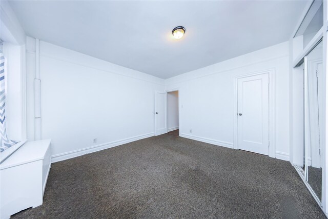 unfurnished bedroom with a closet, baseboards, and dark colored carpet