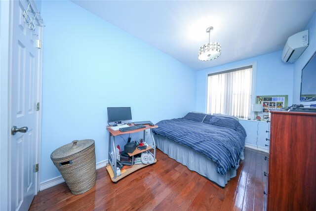 bedroom featuring a wall unit AC, hardwood / wood-style flooring, and baseboards