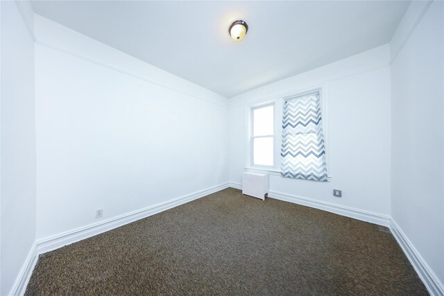 spare room with radiator heating unit, baseboards, and dark carpet