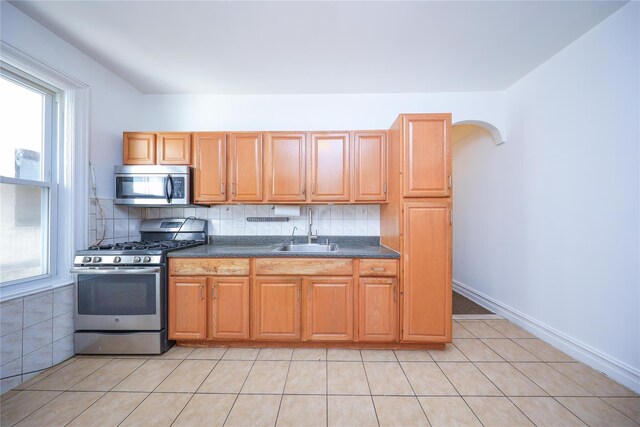 kitchen featuring arched walkways, a sink, stainless steel appliances, dark countertops, and tasteful backsplash