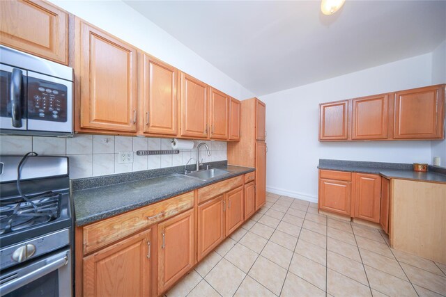 kitchen featuring dark countertops, decorative backsplash, appliances with stainless steel finishes, light tile patterned flooring, and a sink