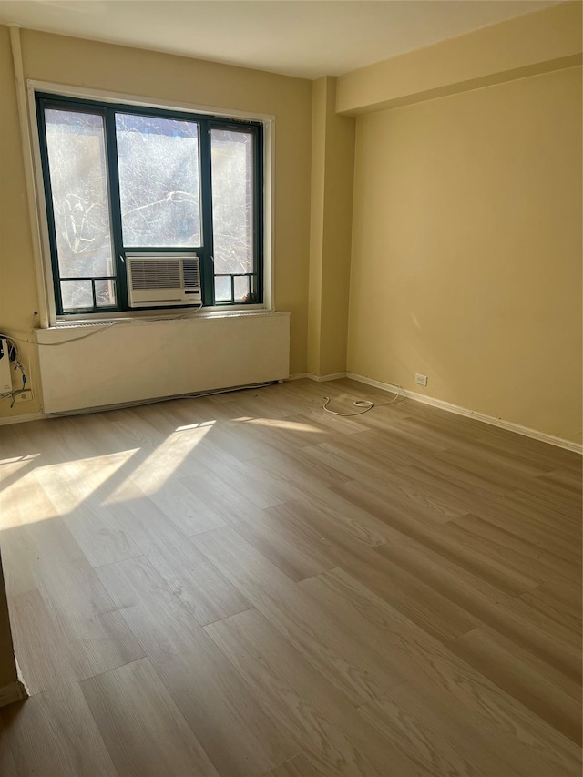 empty room with cooling unit, baseboards, and wood finished floors