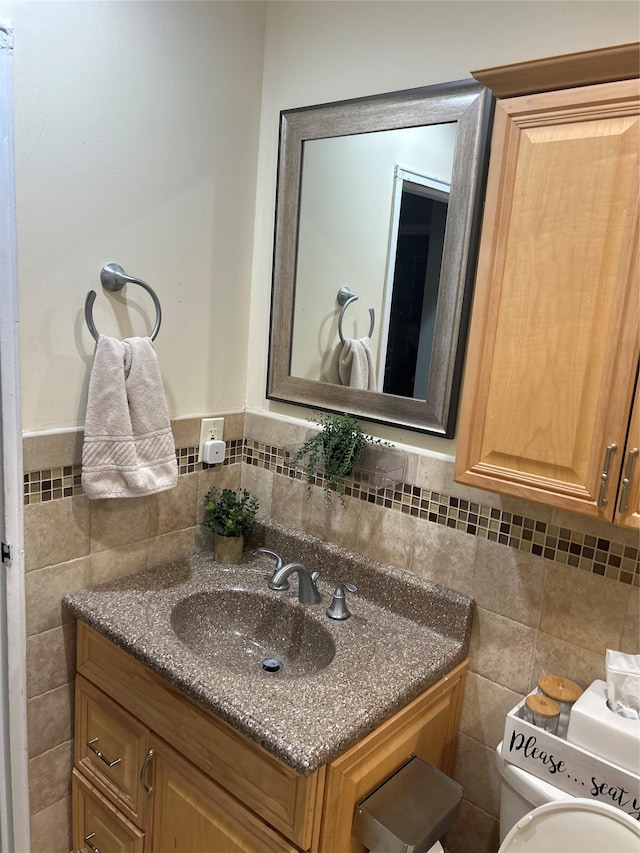 half bath with toilet, a wainscoted wall, tile walls, and vanity