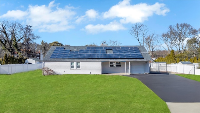 view of front of property featuring aphalt driveway, roof mounted solar panels, fence, a front yard, and a garage