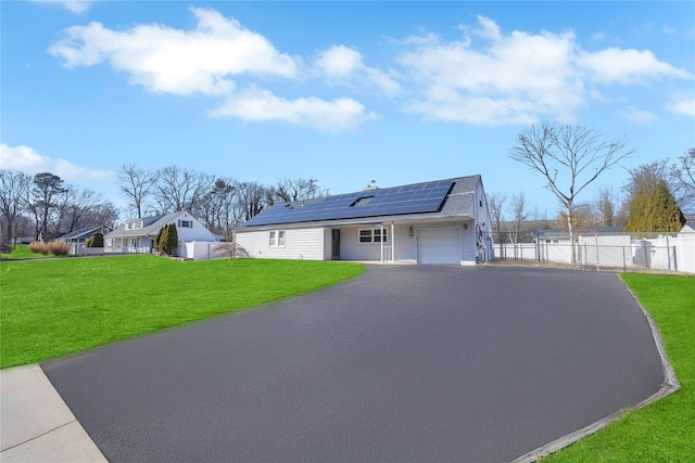 view of front facade featuring a front lawn, aphalt driveway, roof mounted solar panels, fence, and an attached garage