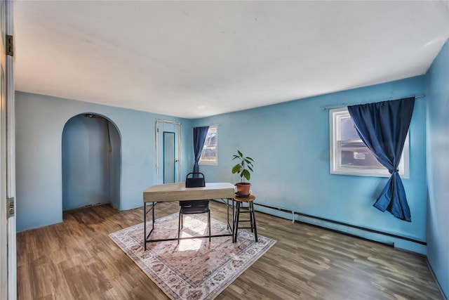 office space with arched walkways, wood finished floors, and a baseboard radiator