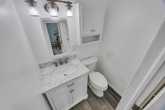 half bath with toilet, vanity, baseboards, and wood finished floors