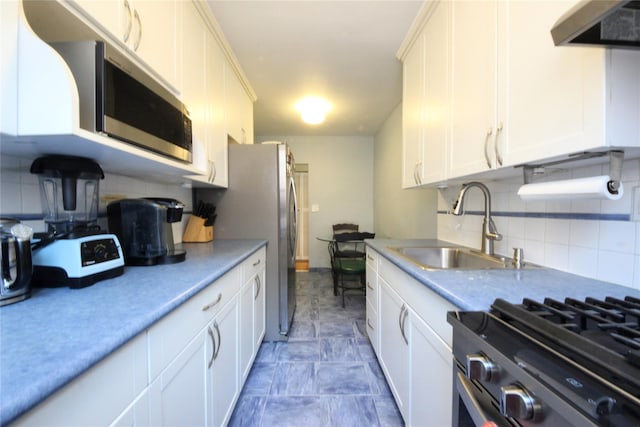 kitchen with tasteful backsplash, wall chimney exhaust hood, appliances with stainless steel finishes, light countertops, and a sink