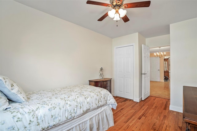 bedroom with light wood-type flooring, a closet, baseboards, and ceiling fan with notable chandelier