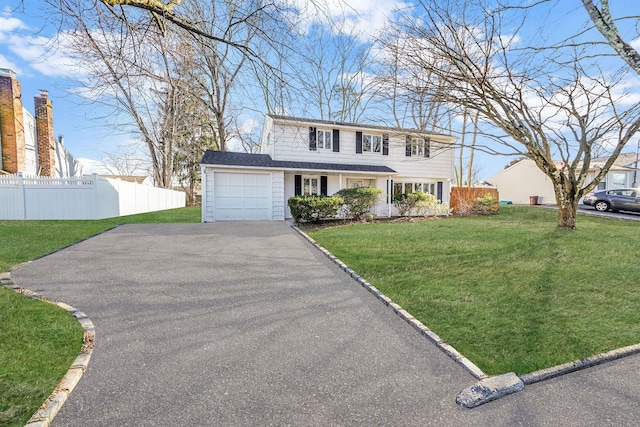 colonial home featuring a front lawn, fence, an attached garage, and aphalt driveway