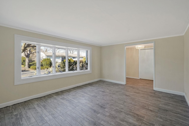 empty room featuring an inviting chandelier, crown molding, baseboards, and wood finished floors