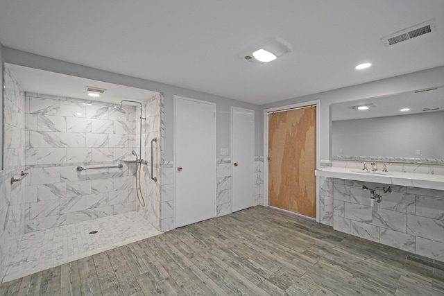 full bath with a tile shower, a sink, wood finished floors, and visible vents