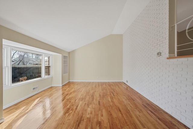 interior space with visible vents, baseboards, lofted ceiling, brick wall, and wood finished floors