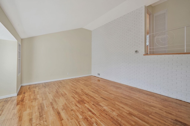 interior space featuring lofted ceiling, baseboards, brick wall, and hardwood / wood-style flooring