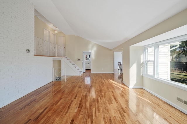 unfurnished living room featuring lofted ceiling, stairway, brick wall, wood finished floors, and baseboards