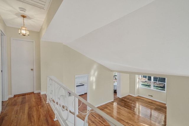 corridor featuring lofted ceiling, visible vents, baseboards, and wood finished floors