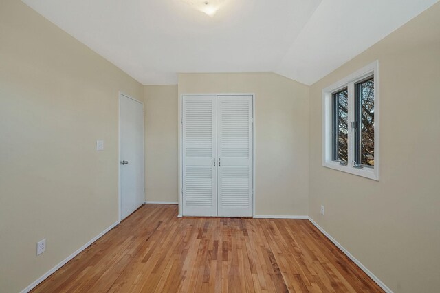 unfurnished bedroom with lofted ceiling, light wood-style floors, baseboards, and a closet