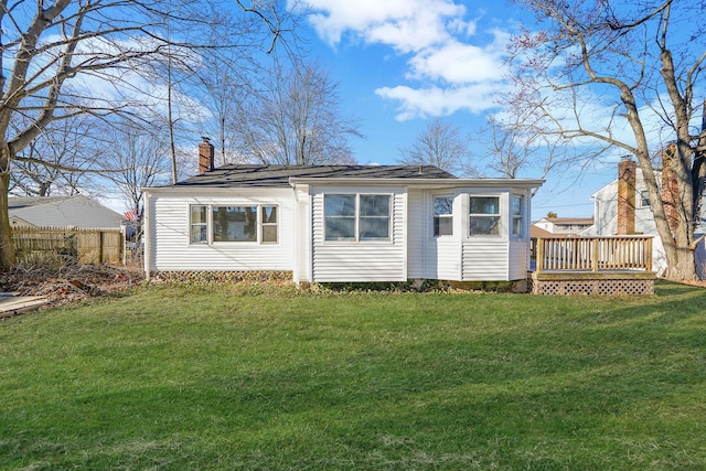 back of property with a wooden deck, a chimney, and a yard