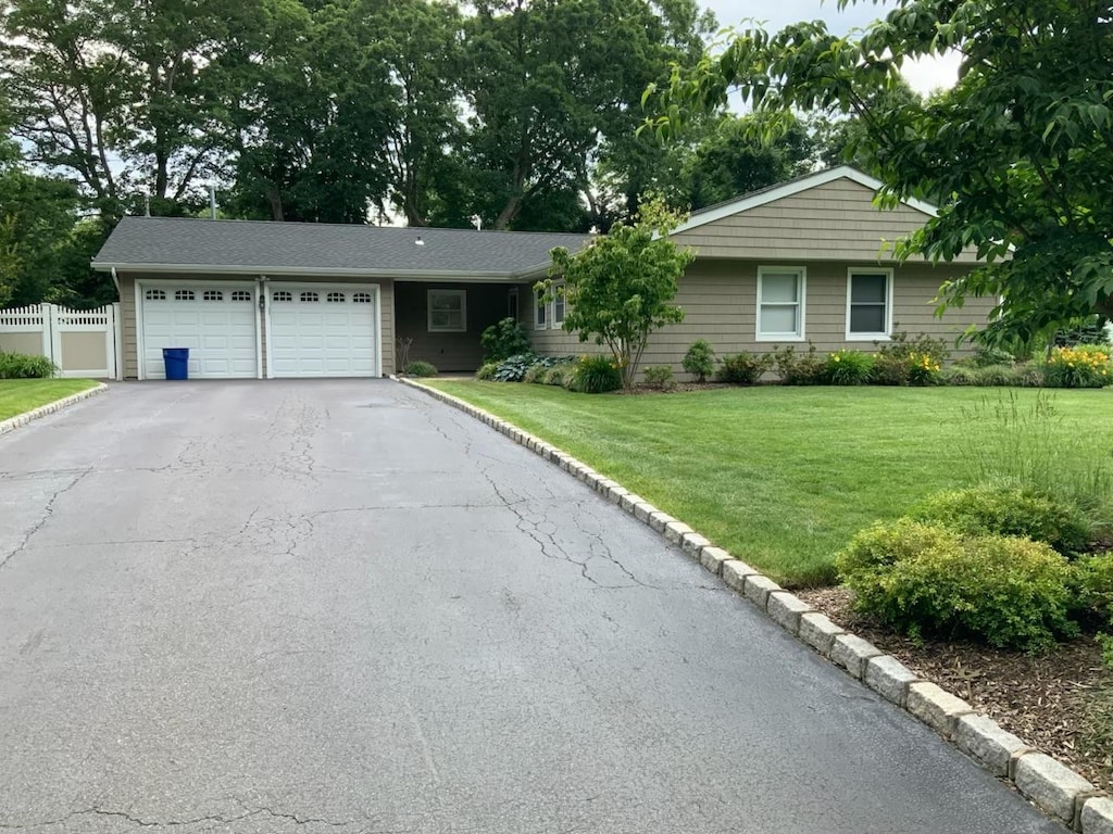 ranch-style home featuring a garage, aphalt driveway, a front lawn, and fence