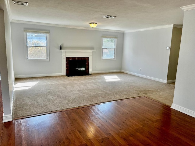 unfurnished living room featuring wood finished floors, visible vents, baseboards, crown molding, and a brick fireplace