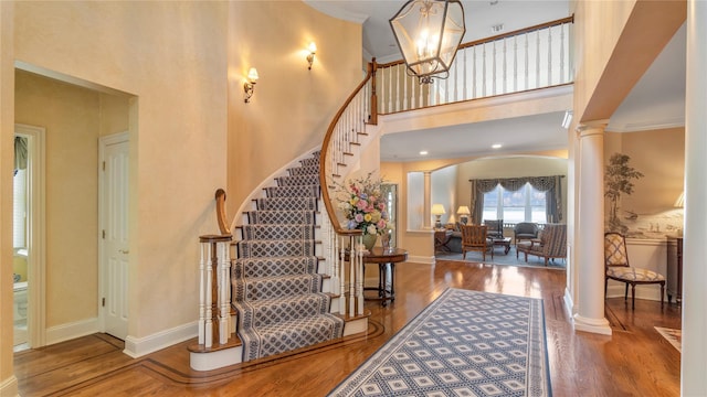 foyer entrance featuring stairway, a high ceiling, wood finished floors, baseboards, and decorative columns