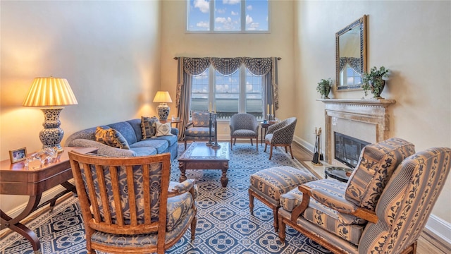 living area featuring a fireplace with flush hearth, wood finished floors, a towering ceiling, and baseboards
