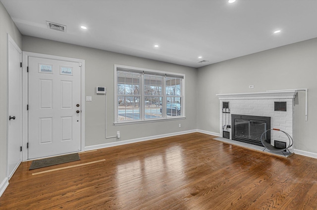 unfurnished living room with baseboards, visible vents, wood finished floors, a brick fireplace, and recessed lighting