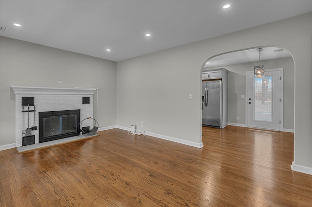 unfurnished living room with arched walkways, a fireplace, recessed lighting, and wood finished floors