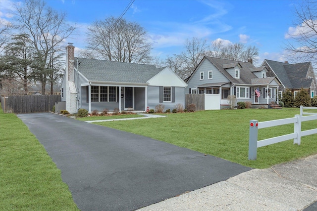 view of front of property with aphalt driveway, roof with shingles, a chimney, fence, and a front lawn