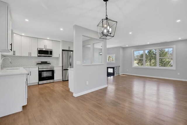 kitchen featuring a sink, open floor plan, appliances with stainless steel finishes, light wood-type flooring, and backsplash