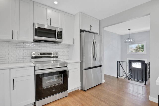 kitchen with light countertops, light wood-style floors, appliances with stainless steel finishes, white cabinetry, and tasteful backsplash